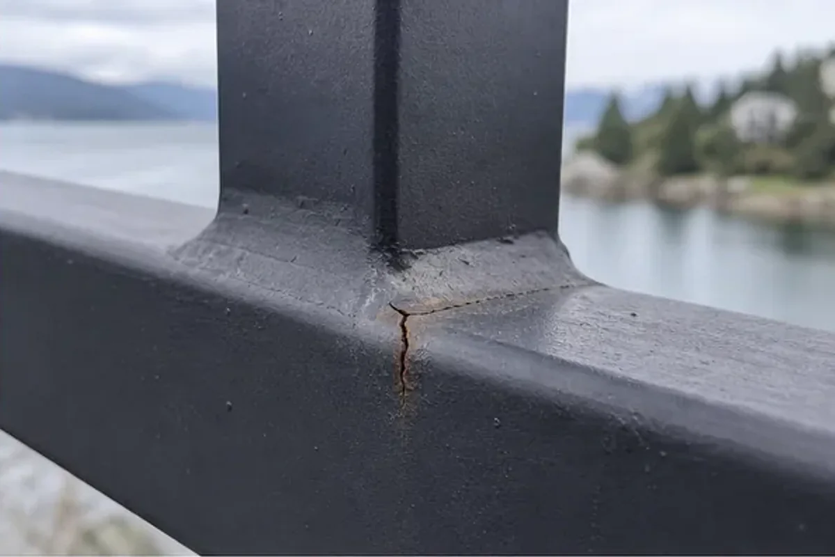 Cracked weld where a black steel deck railing post meets the horizontal rail