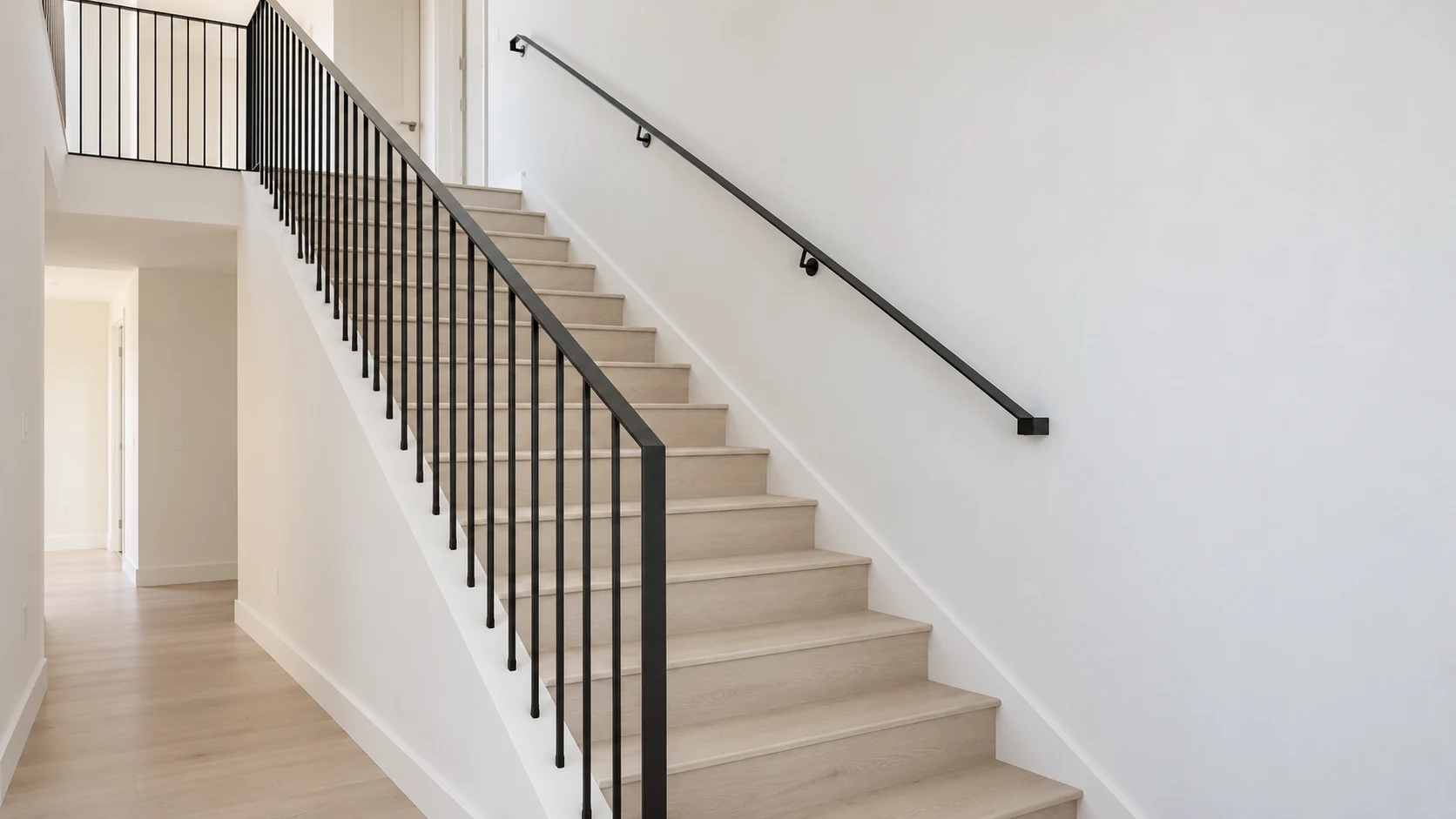 Slender black vertical-picket railing beside a light oak interior staircase and upper landing.