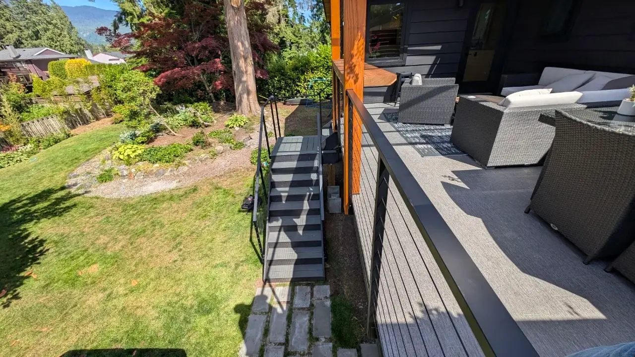 View along the slim matte black top rail of the deck cable railing toward the staircase and garden below