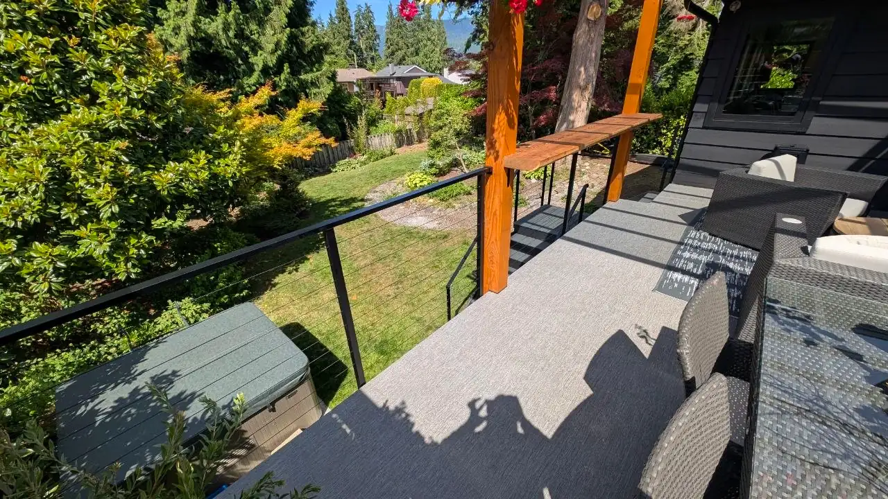 Deck-level view through the horizontal stainless cables toward the backyard, hot tub visible below the rail