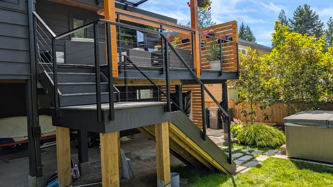 Powder-coated stainless cable railing wrapping the stair landing, with the lower flight continuing down to the backyard lawn