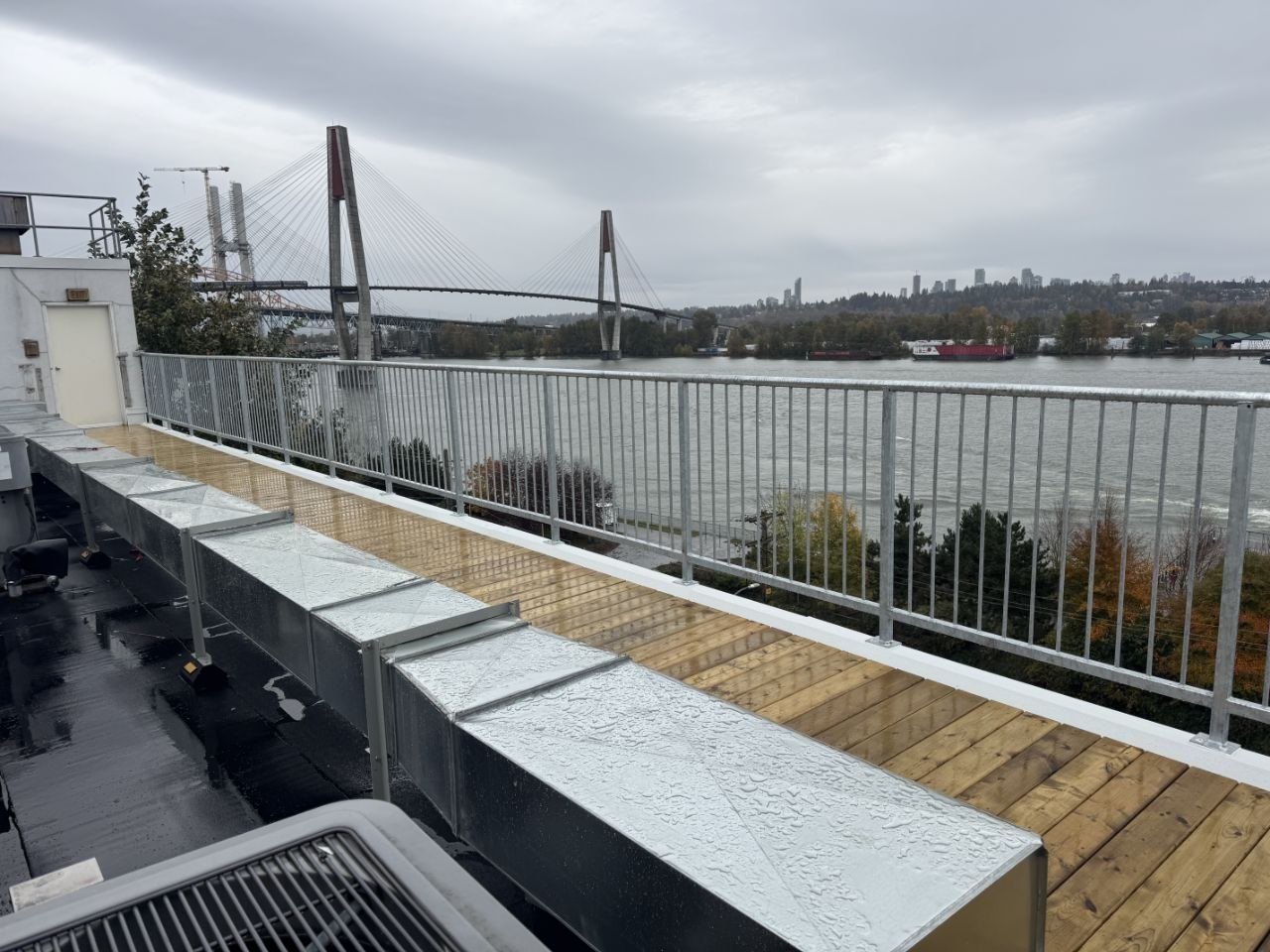 Commercial rooftop install — galvanized guard rail at a building edge overlooking the Skytrain bridge over the Fraser River, by LOUEI Metal Arts