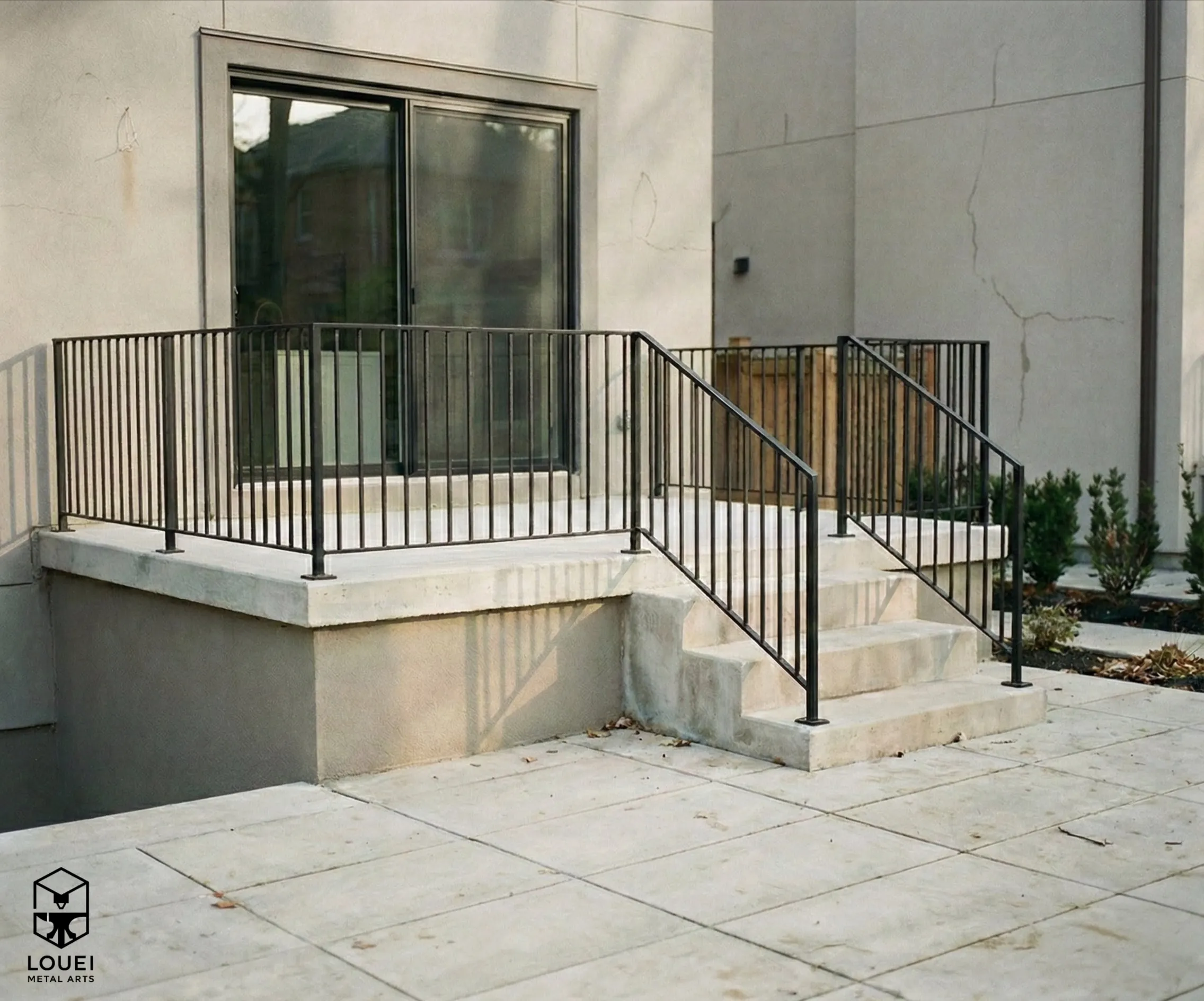 Black metal picket railing around raised concrete patio and entry steps at a Vancouver home