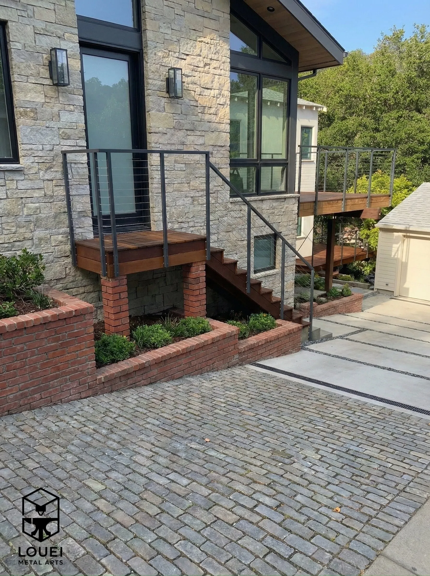 Exterior cable railing with black metal posts and horizontal cable infill on wood deck stairs at a modern stone home.