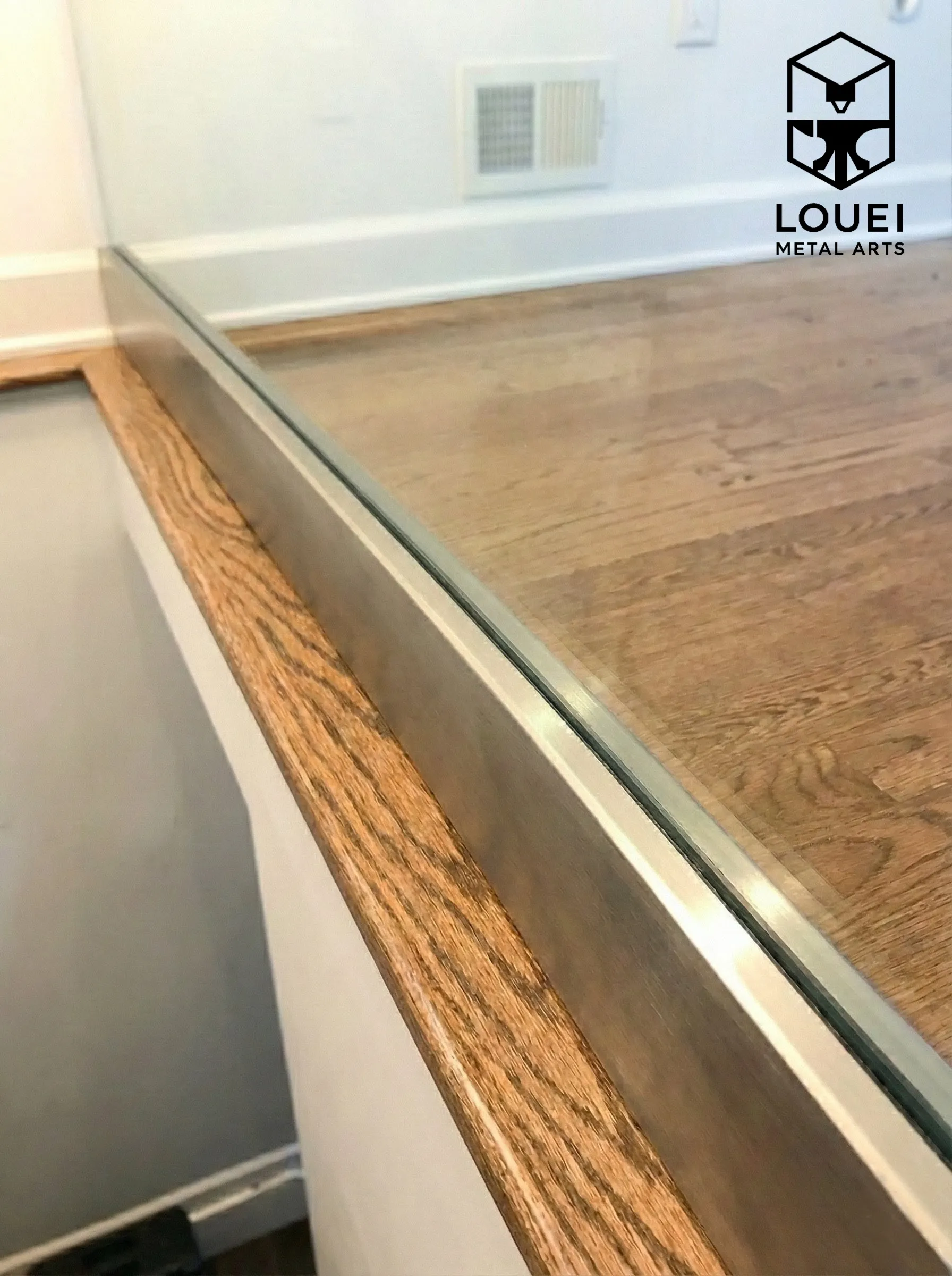 Close-up of a frameless glass railing set in a brushed stainless base-shoe channel along a wood stair opening trim.