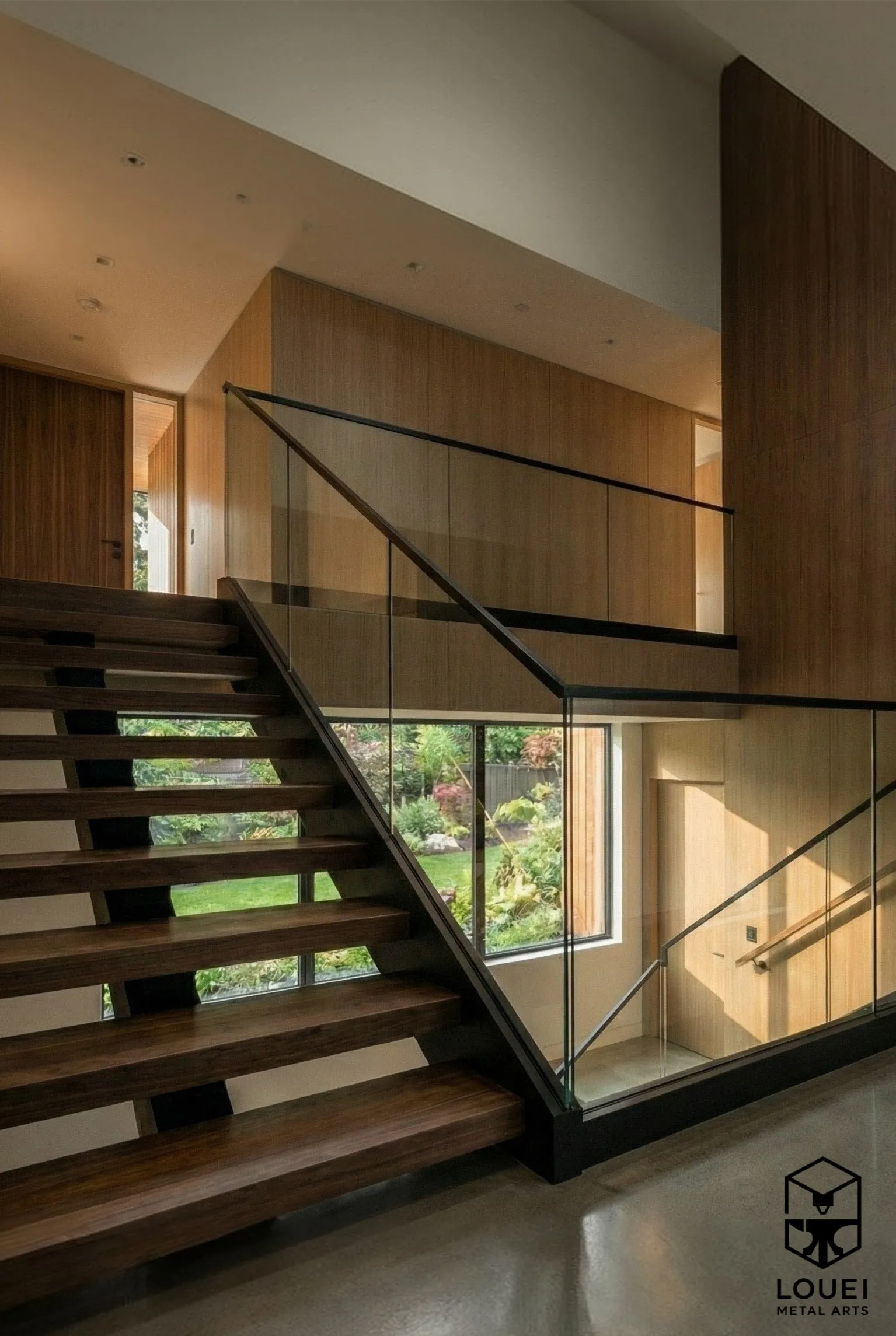 Interior glass stair railing with a black handrail alongside an open-riser wood staircase and upper landing.