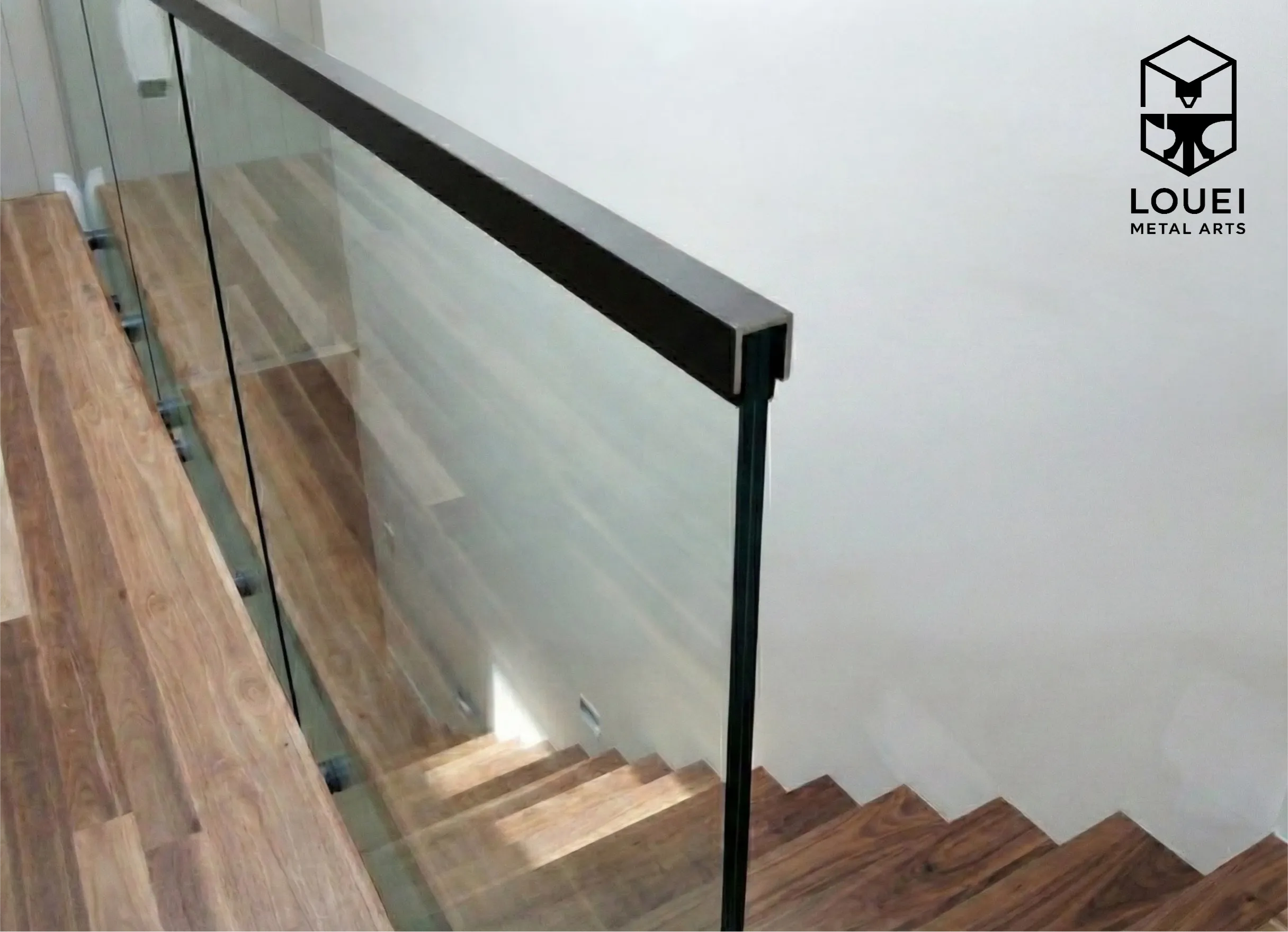 Interior glass stair railing with a black square cap rail alongside wood stair treads.