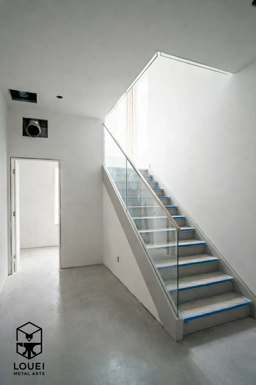 Interior glass stair railing with a stainless steel top rail on a straight staircase.