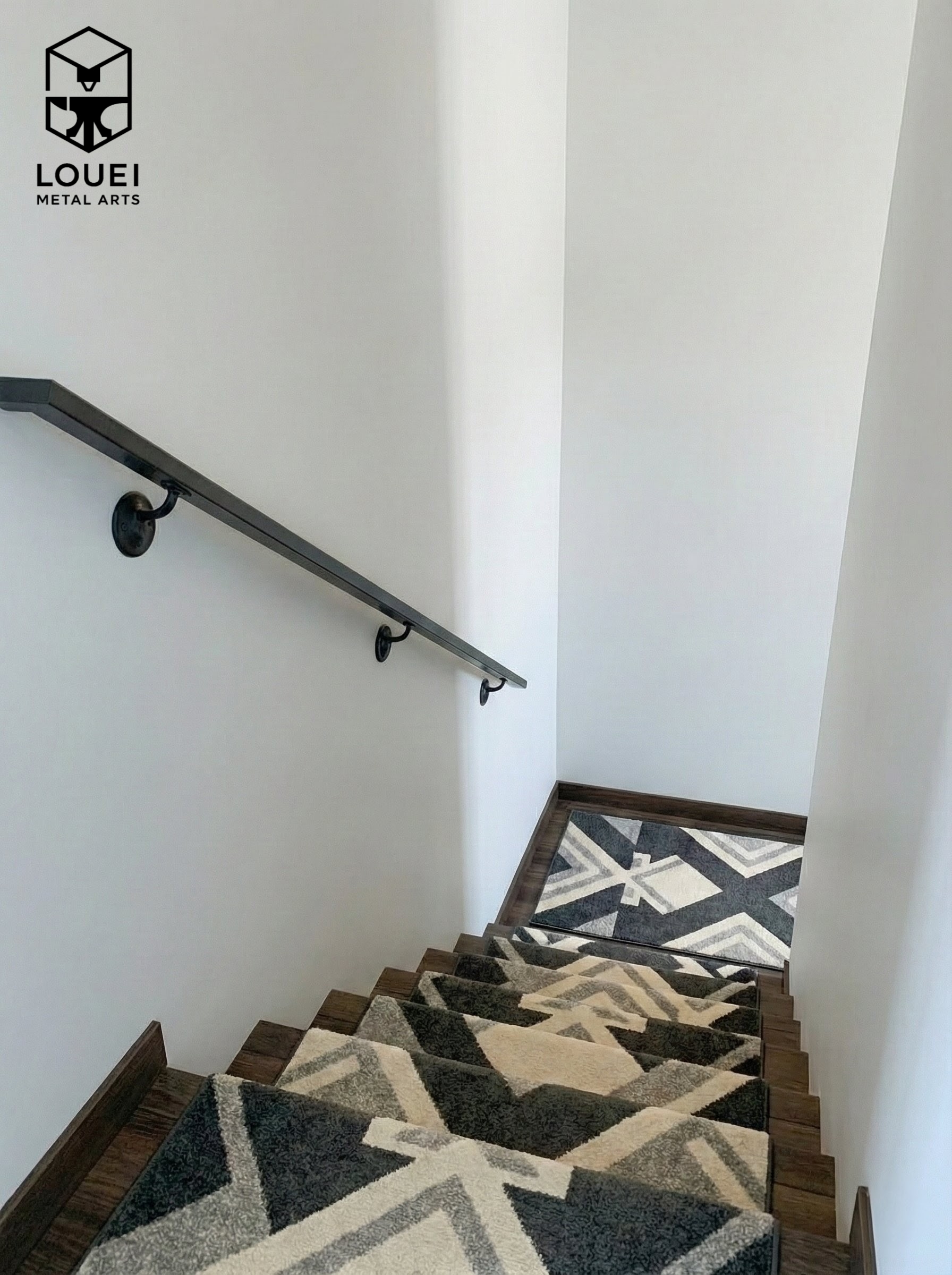 Wall-mounted black steel handrail along an interior Vancouver staircase with a patterned runner.