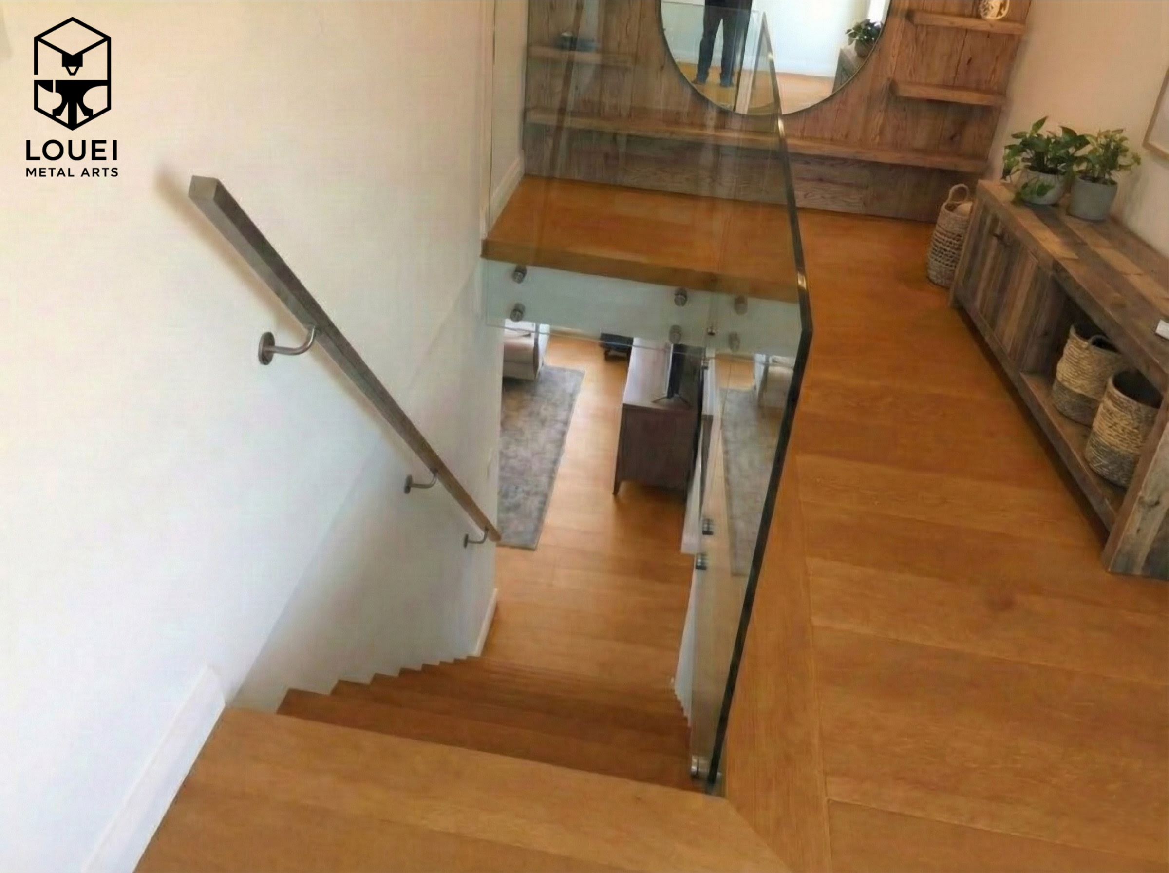 Wall-mounted stainless steel rectangular handrail along an interior wood staircase with a glass guardrail at the stair landing.